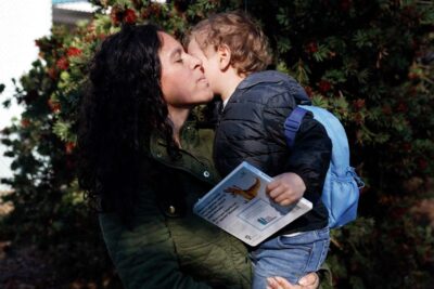 A woman kisses a child on the cheek while showing a book—representing love and learning.