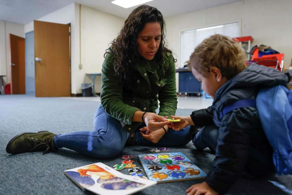 A woman and a child play with a puzzle on the floor—emphasizing early education and bonding.