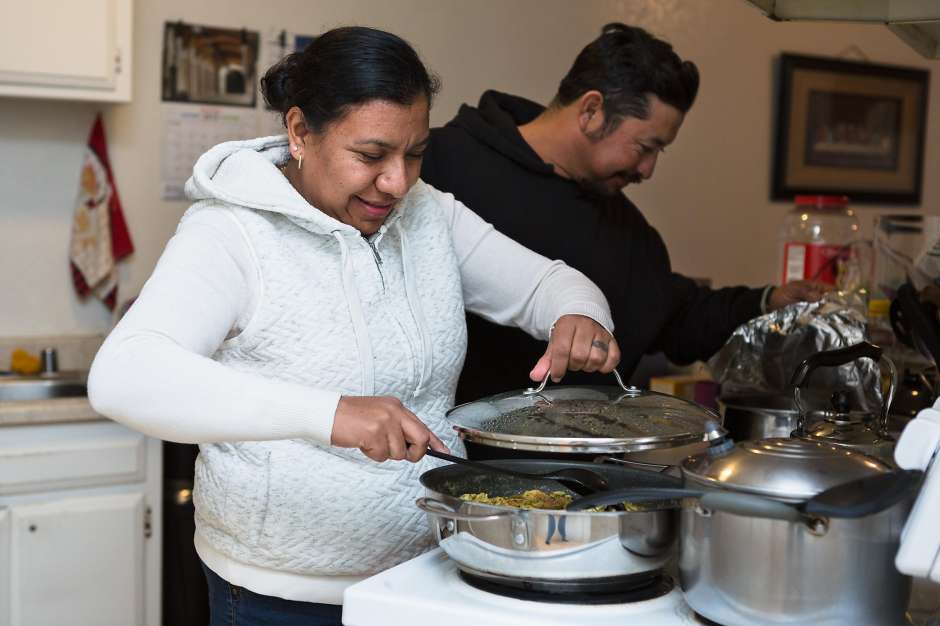 Couple cooks meal in kitchen while smiling.
