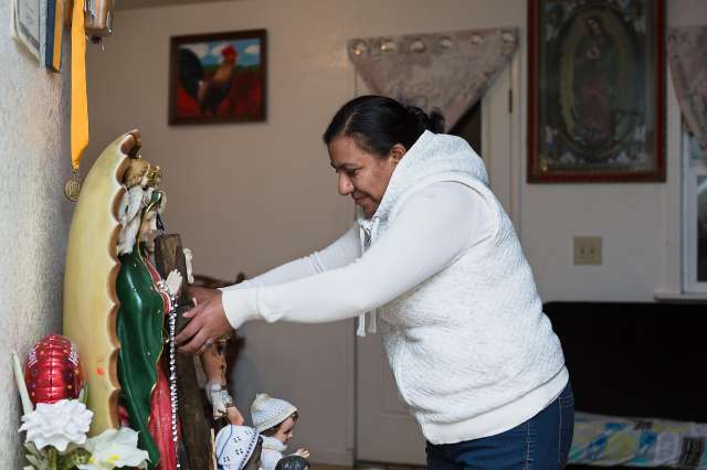 Woman dusts religious statue displayed at home.