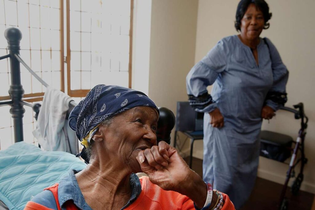 Elderly woman smiling joyfully as daughter stands in background.