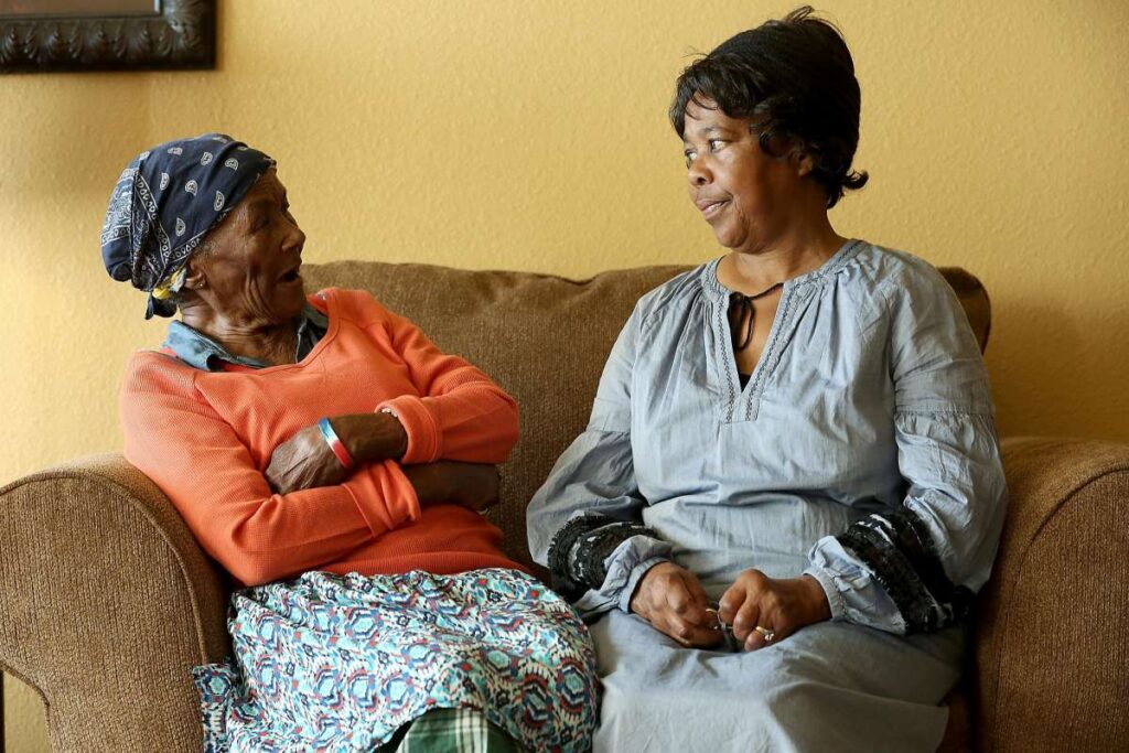 Elderly woman smiling joyfully with daughter on couch.