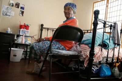 Elderly woman seated in a chair looking peaceful, hands folded.