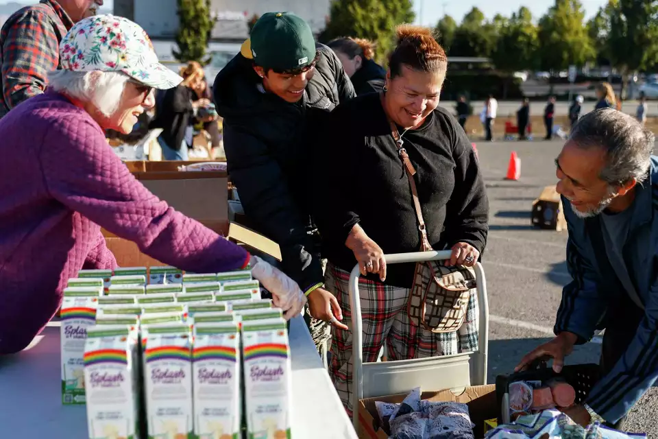 A woman pushes a cart with groceries alongside volunteers—capturing dignity and mutual aid.