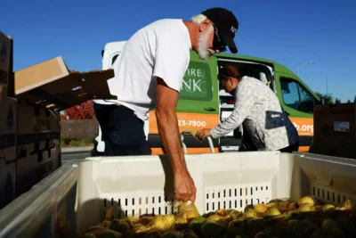Two volunteers load produce into crates from a truck—highlighting food distribution and community service.