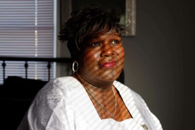 A woman with a patterned dress sits calmly in a softly lit room—conveying dignity and presence.