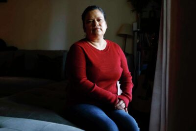 A woman in a red sweater sits calmly, hands folded—conveying warmth and presence.