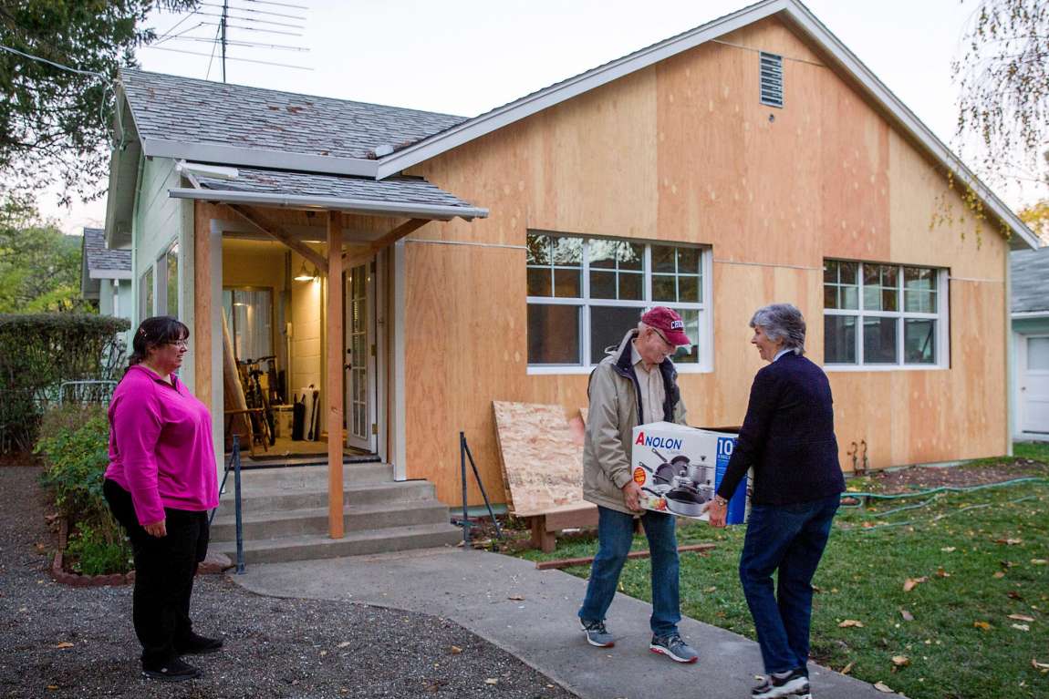 Woman smiles while movers carry household items into new home.