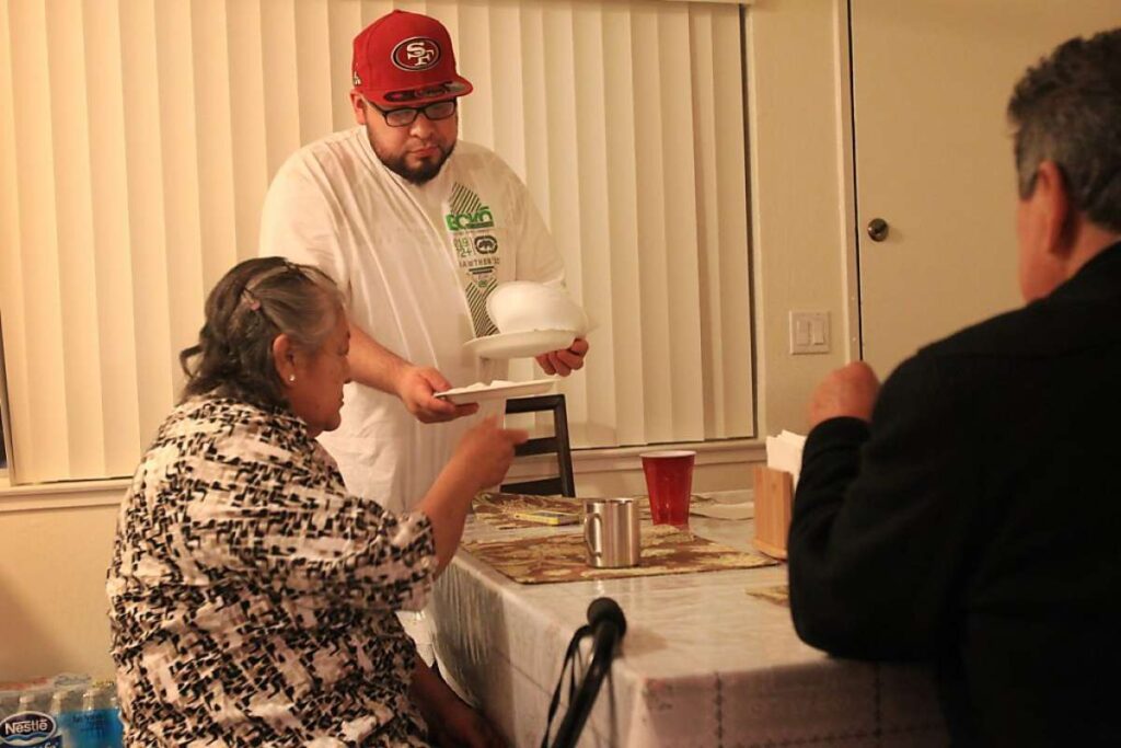 Man helps elderly woman clean up dishes at table.