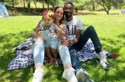 A family of three sits on a picnic blanket in a sunny park, smiling and relaxed—showcasing joy and togetherness.