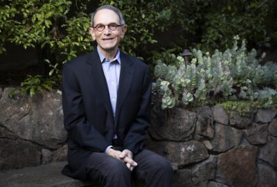 A man in a suit smiles while seated beside a succulent garden—conveying professionalism and approachability.