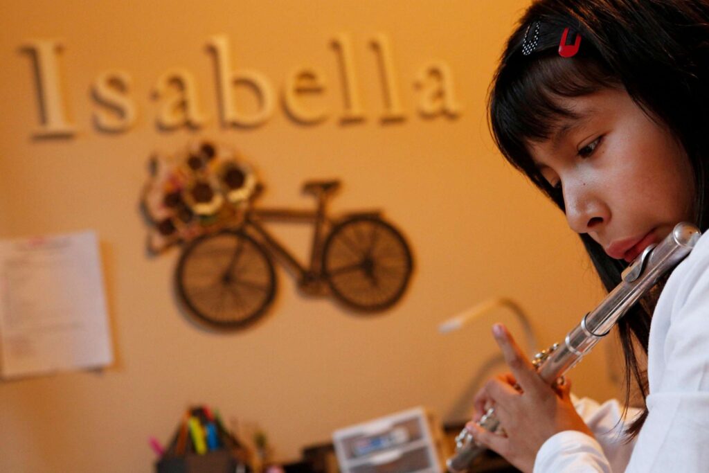 Child plays flute in room with wall art with the name "Isabella" and a bicycle design.