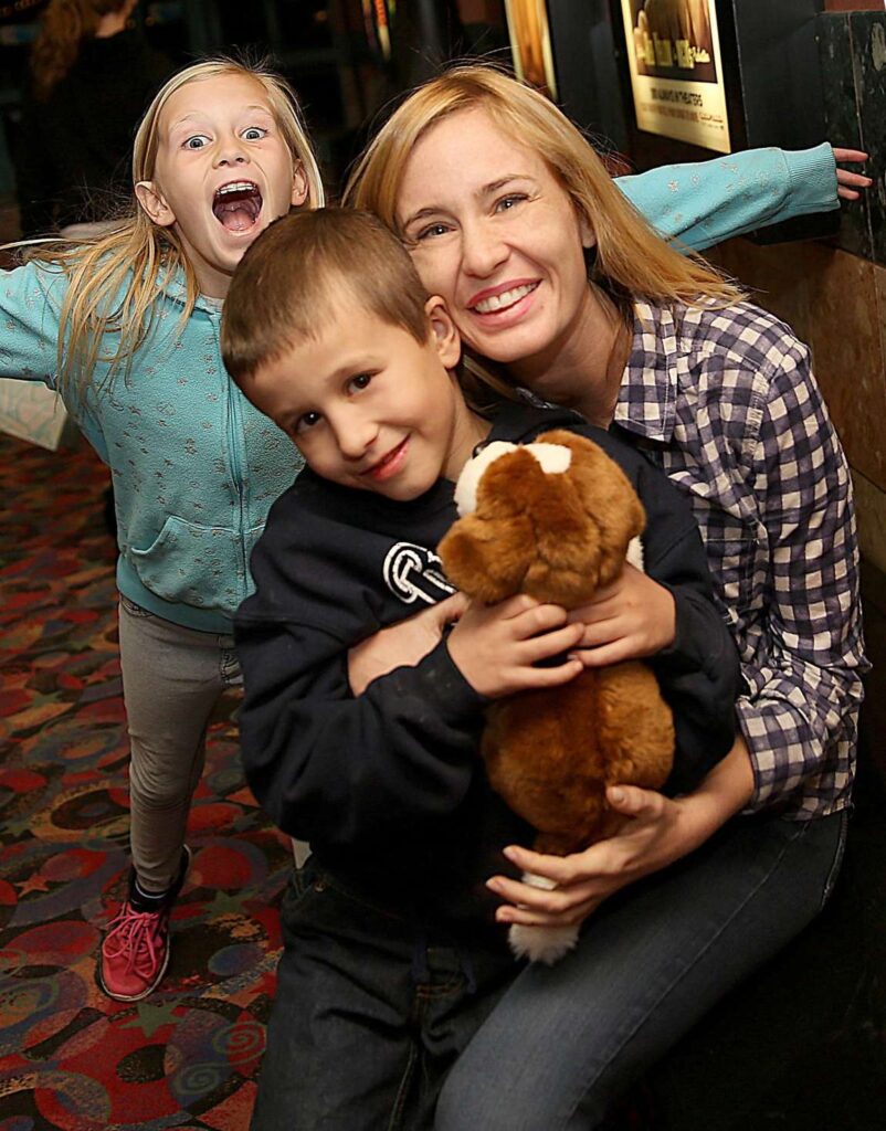 Woman smiling and hugging two children with a puppy.