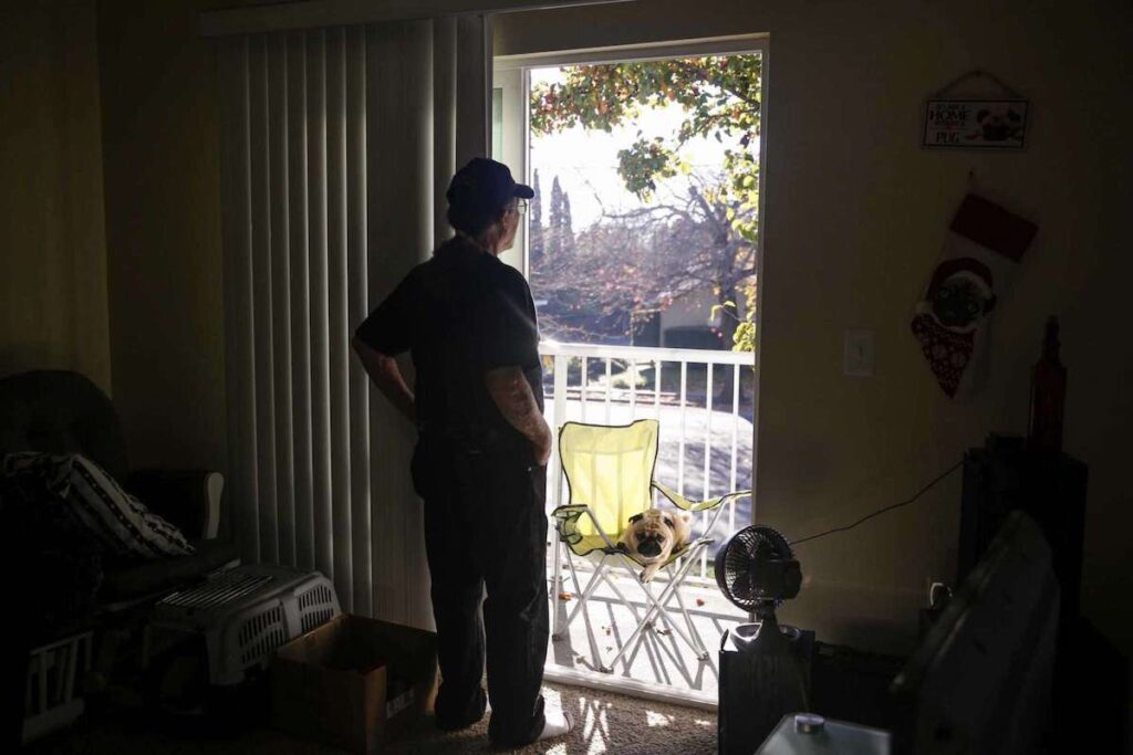 A man stands near a sliding door looking out to his dog—symbolizing quiet reflection at home.