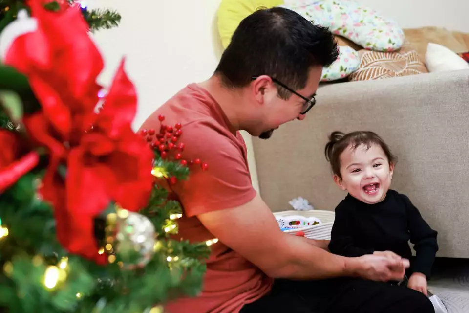A father and child laugh together near a Christmas tree—sharing joyful family moments.
