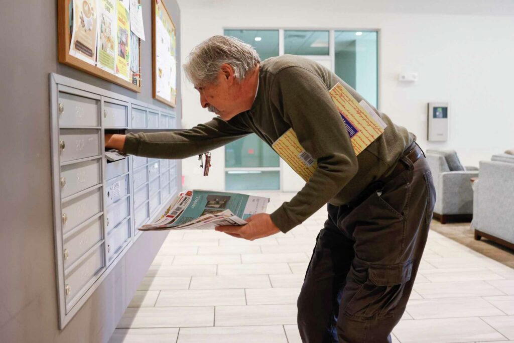 A man leans down to gather mail from PO box—illustrating routine and responsibility.