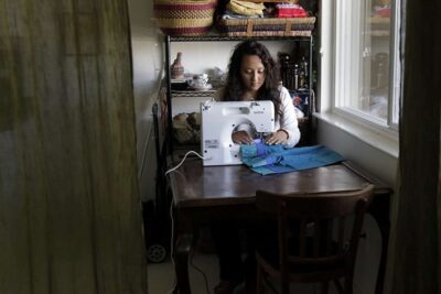 Woman sitting at desk using sewing machine.