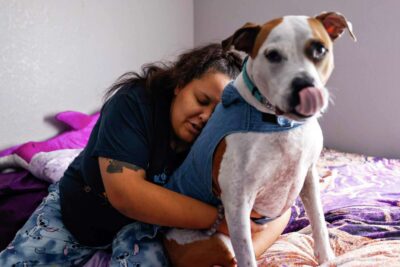 A woman hugs her dog lovingly while sitting on a bed—showing companionship and trust.