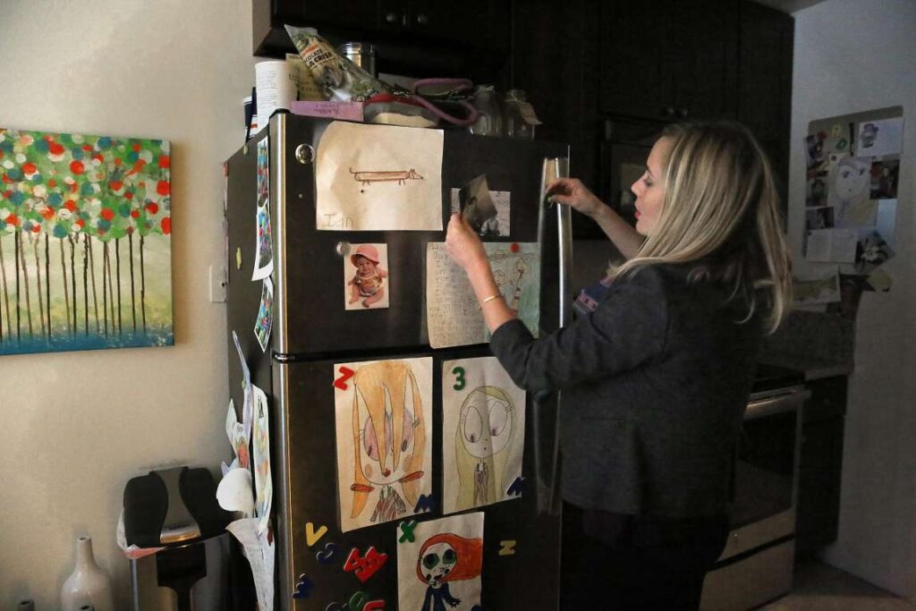 Woman decorating refrigerator with children's drawings with magnets.
