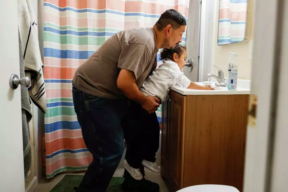 A man helps a child wash their hands at a sink—demonstrating care, safety, and parenting.