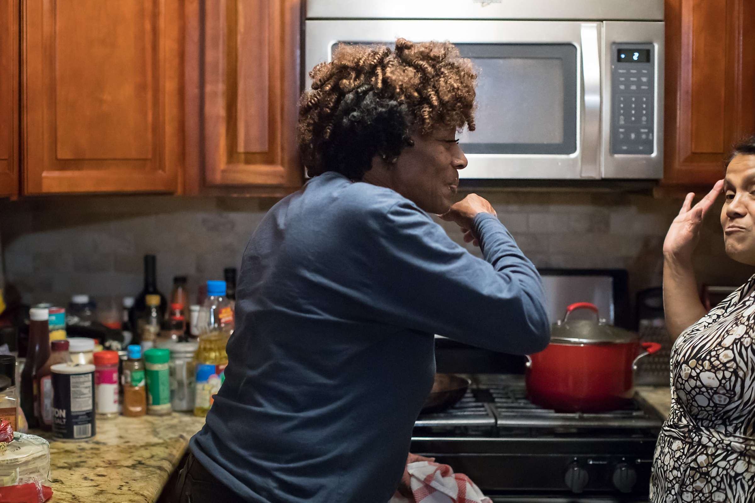 Woman cooking at a stovetop while another adult observes.