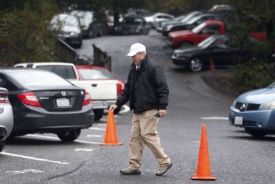 Elderly man walking across a parking lot placing traffic cones for direction.