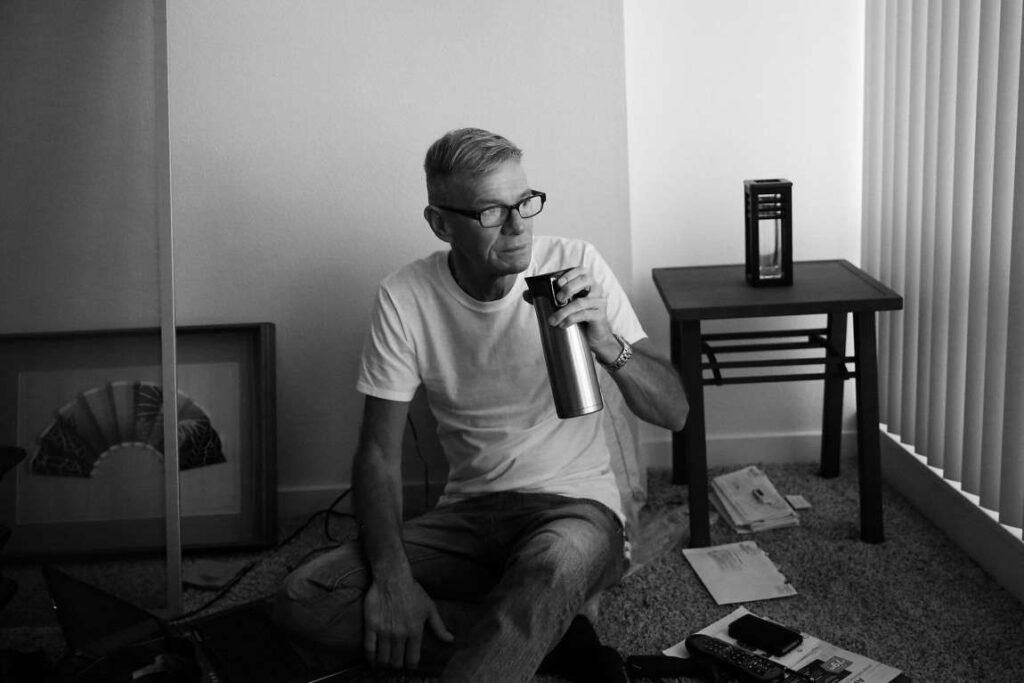 Man seated on floor and sipping coffee out of thermos.
