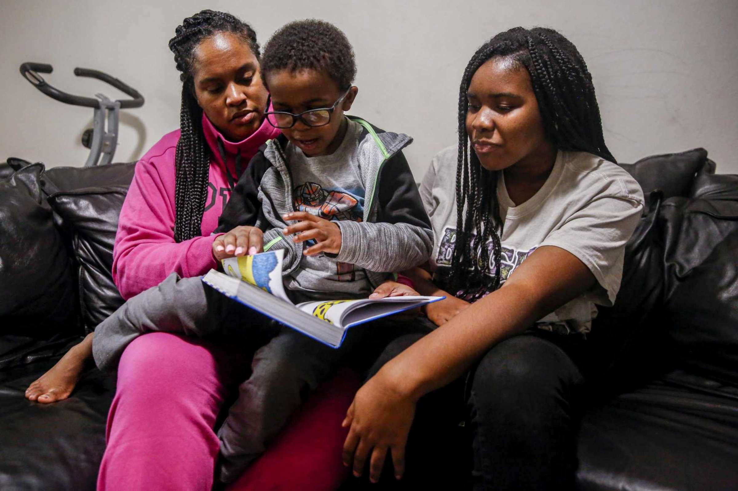 A woman reads with two children on a couch—portraying learning, literacy, and family togetherness.