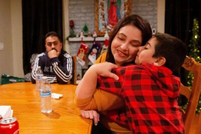 Woman embraces a smiling child at a table during a holiday meal.