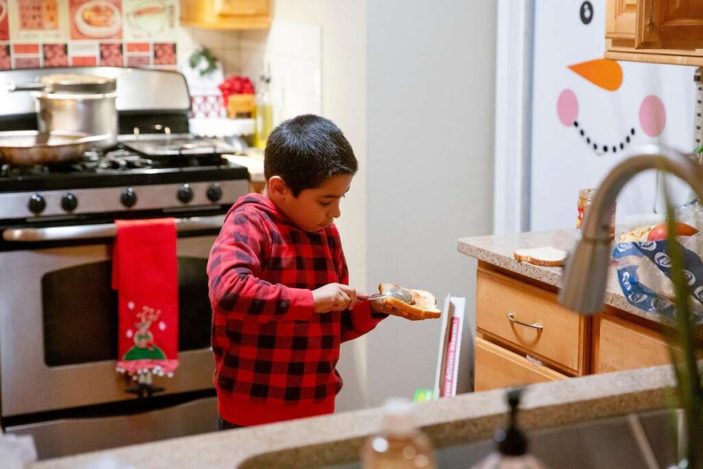 Child focused on making a sandwich in a kitchen with holiday decorations.