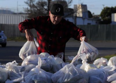 A man in a red plaid shirt sorts plastic bags full of food—representing preparation and community service.
