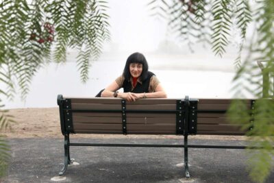 Woman sits on a bench in a park, looking reflective.