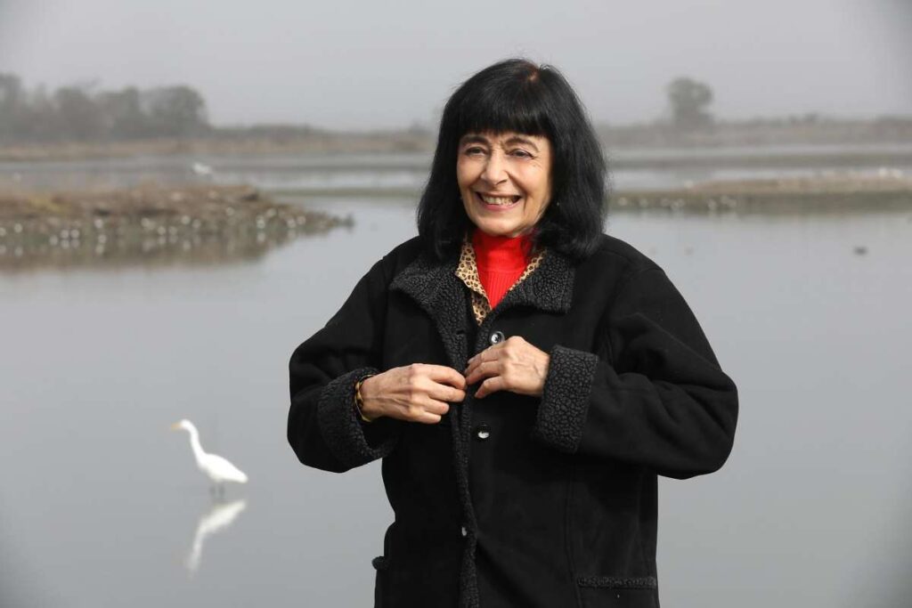 Woman smiles while standing near a lake on a cloudy day.