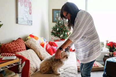 A woman reaches down to pet a small dog near a Christmas tree—reflecting warmth and companionship during the holidays.
