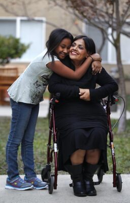 Woman in wheelchair being hugged by child.