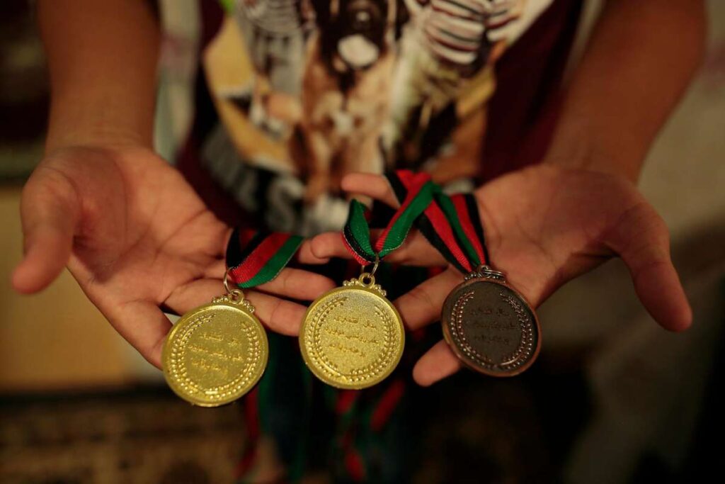Close-up of medals and ribbons held up proudly in someone’s hand.