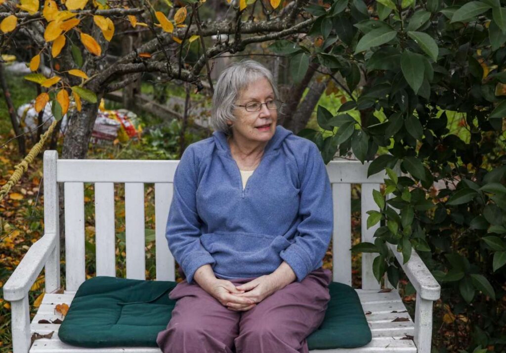An older woman sits on a bench outdoors, smiling gently—expressing wisdom, calm, and presence.