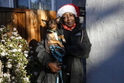 A woman in a winter hat holds a small dog—portraying warmth and companionship.