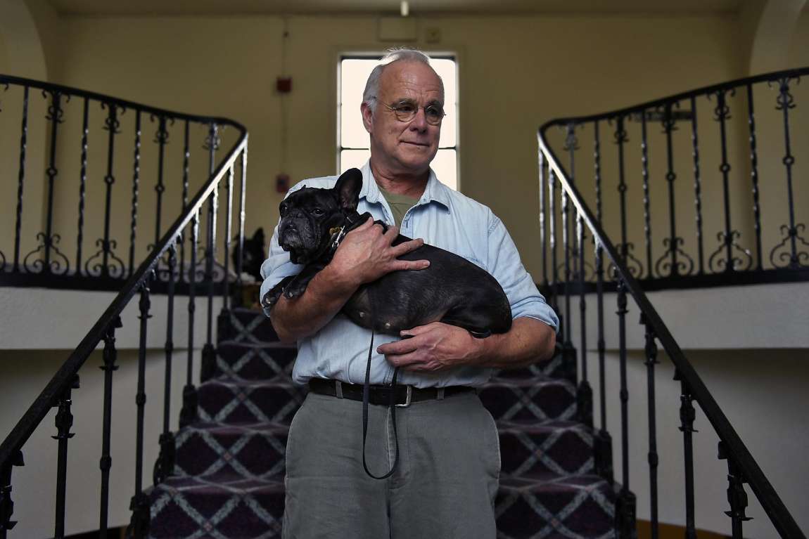 Elderly man holding small dog on stairway.