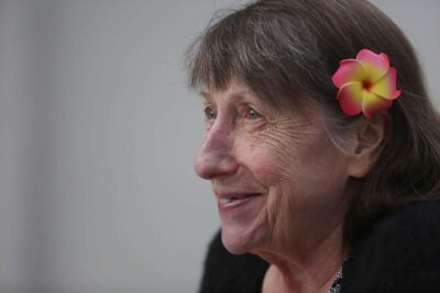 Portrait of an older woman with a flower tucked behind her ear, smiling softly.