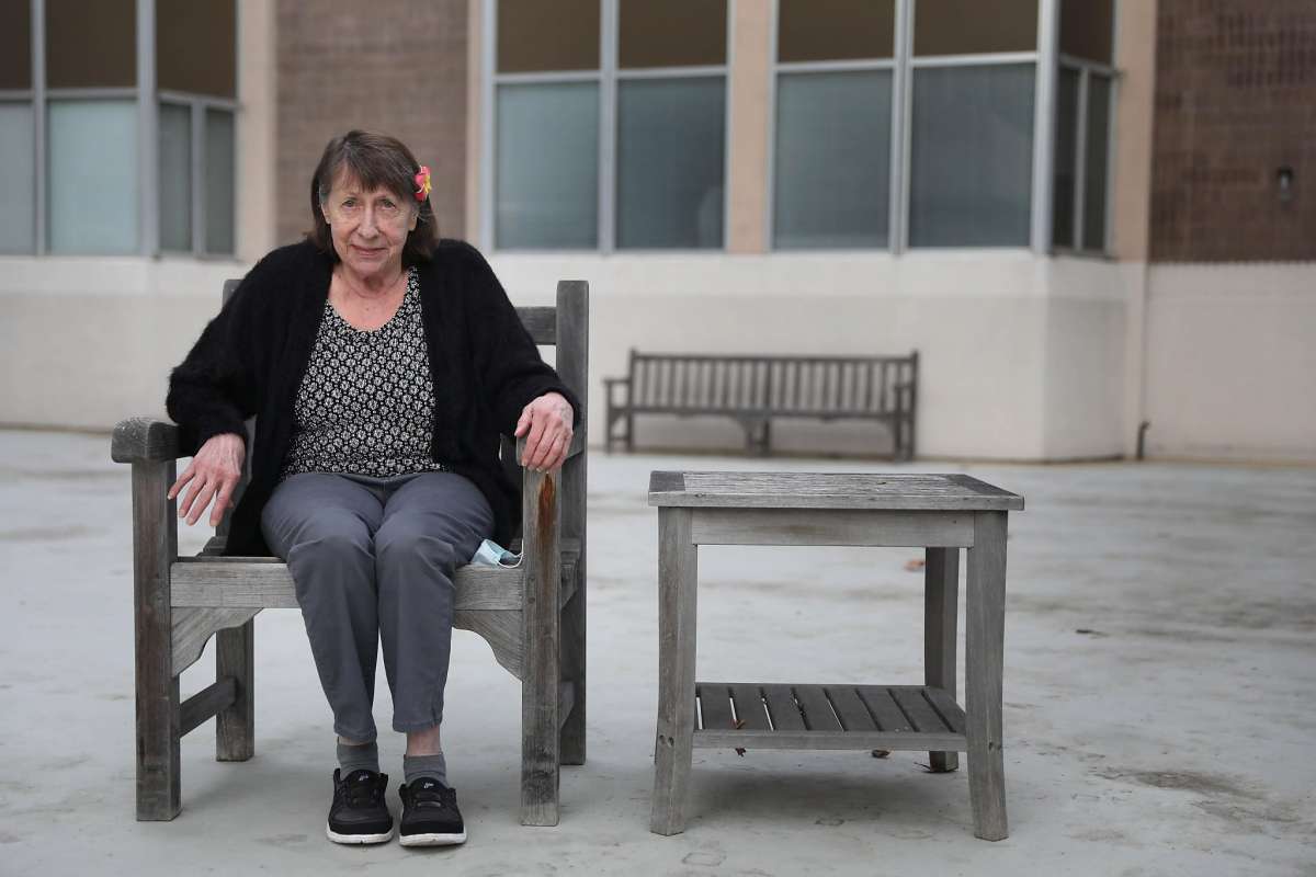 Woman sits on a bench in a courtyard area, looking calmly ahead.