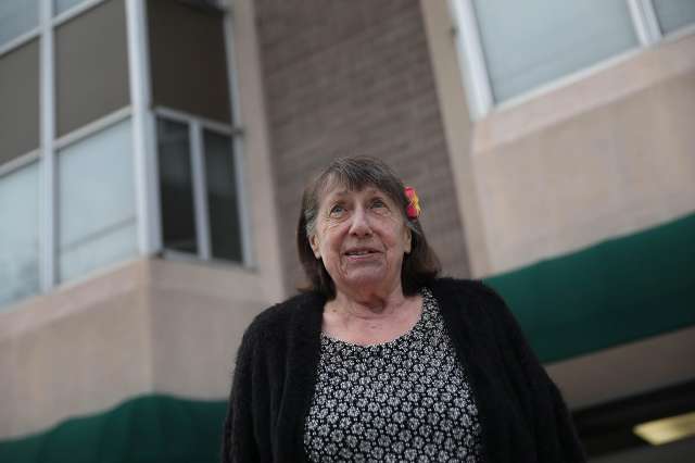 Older woman stands outside a residential building, smiling gently.