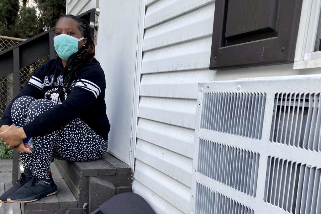 Woman in a mask sits on steps outside her home.