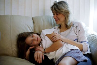 Mother embraces daughter on couch while smiling.
