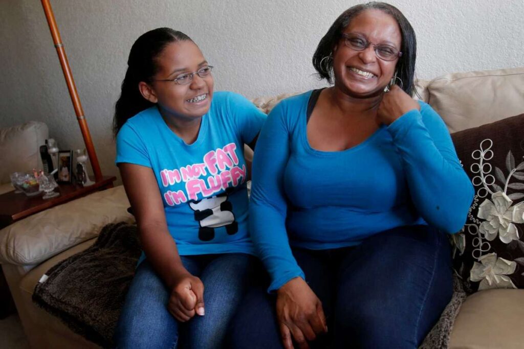 Mother and daughter laugh while posing for photo on couch.