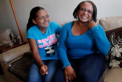 Mother and daughter laugh while posing for photo on couch.