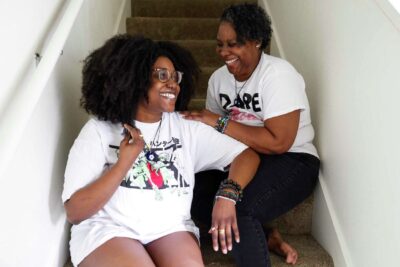 Two women laugh together while sitting on stairs—celebrating joy and togetherness.