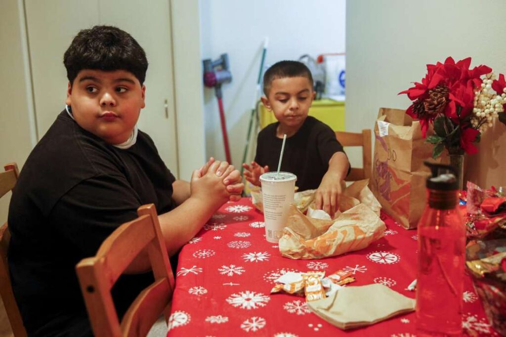 Two children sit at a red table eating and talking—depicting everyday family life and connection.