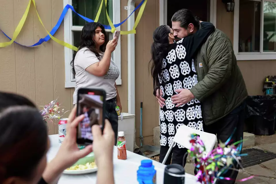 A man and woman greet each other with a warm hug at a decorated front door—symbolizing hospitality and reunion.