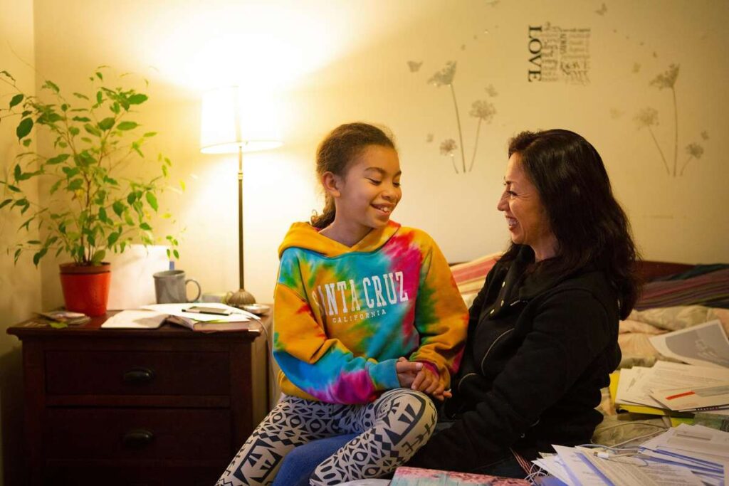 Child in colorful hoodie sitting with a woman in a cozy room.